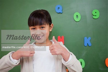 Happy schoolgirl with the thumbs up in front of a blackboard