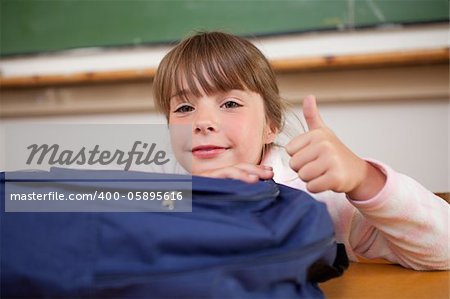 Schoolgirl posing with a bag and the thumb up in a classroom