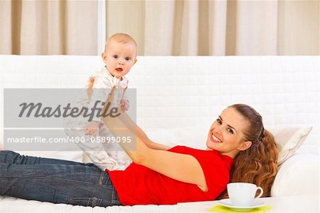 Smiling mother and adorable baby playing on couch