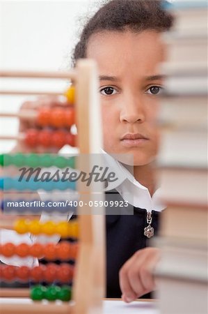 A beautiful young mixed race African American girl reading in a school classroom with a pile of books in front of her using an abacus