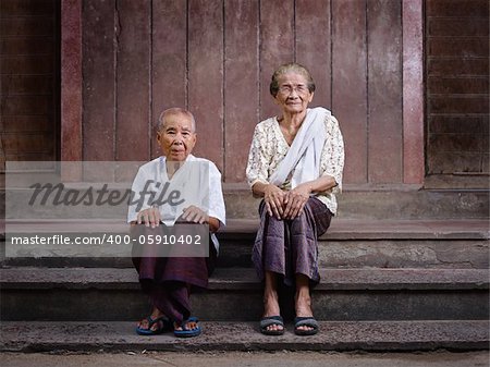 Portrait of two old asian women sitting on steps out of their house and looking at camera