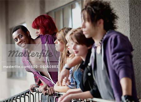 A group of young punk rock teens stare into distance as attractive African American teen smiles towards camera.