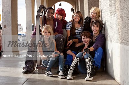 A group of attractive young teen punks sit on a set of stairs while hanging out.