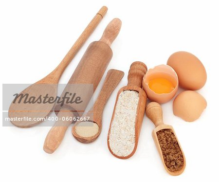 Brown wholegrain flour, eggs and sugar with natural wood baking utensils over white background.