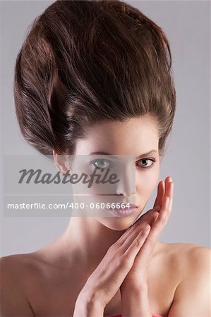 close up portrait of young alluring girl with dark hair and creative hairstyle posing on gray background