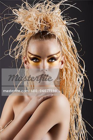 close  up of an amazing woman in ethnic style with creative make up and raffia on the head doing hairstylish. She is in front of the camera, looks in to the lens and has the right hand on the left shoulder