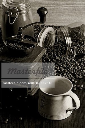 Photo of roasted coffee beans, coffee cup, antique grinder on a wooden table.