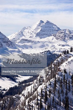 A winter landscape view, in vertical format, of the two peaks in the Maroon Bells massif in Colorado.