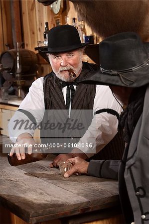 Serious bartender with cigar pours drink for customer