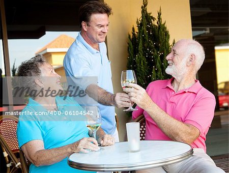 Waiter serving wine to a senior couple at a restaurant.