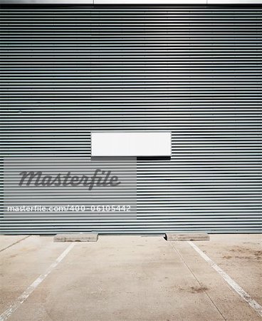 Concrete parking floor and tin wall with blank info board.