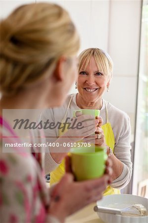 Happy women in home kitchen: mom and daughter talking and drinking a cup of tea