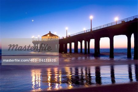 Manhattan Beach California Pier at twilight. Moon and a few stars visible in the background. Pier lights reflecting on the sand.