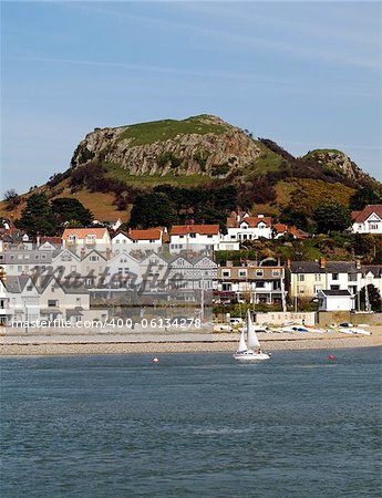 A yacht sailing along the Afon Conwy, at Deganwy, North Wales.  The hill in the background was once the site of Degannwy castle, now only the ruins remain.