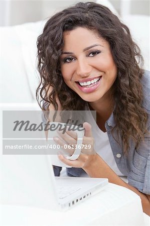 Beautiful young Latina Hispanic woman smiling, relaxing and drinking a cup of coffee or tea using laptop computer