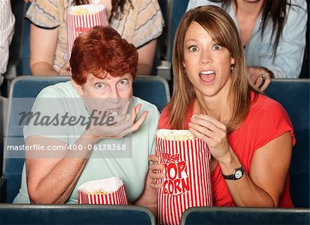 Scared Caucasian ladies in theater eating popcorn