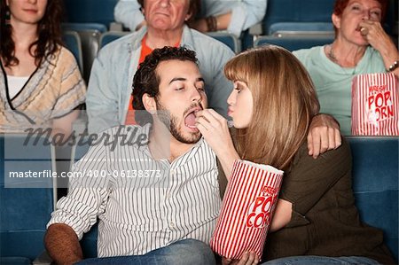 Loving young girlfriend feeds boyfriend popcorn in a theater