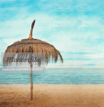 Straw parasol with cloudscape and calm sea water on sand beach on a tropic island