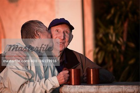 Senior woman kisses happy man in hat outdoors