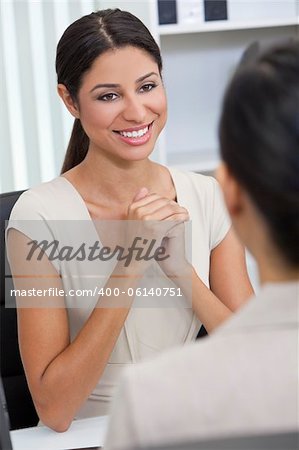 Beautiful young Latina Hispanic woman or businesswoman in smart business suit sitting at a desk in an office having a meeting