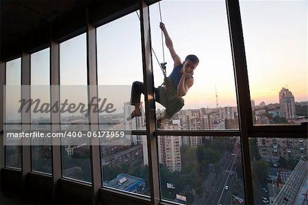 Industrial climber looking through a window while hanging on a rope outside a high building