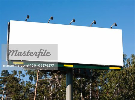 Blank billboard against blue sky and green trees