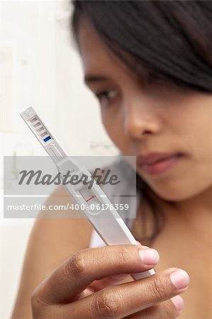 Sullen Asian woman holding negative result pregnancy test device.