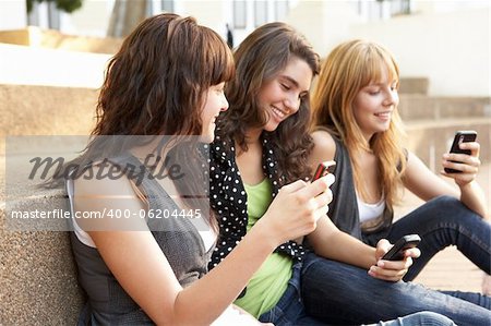 Group Of Teenage Students Sitting Outside On College Steps Using Mobile Phone