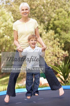 Grandmother And Grandson Jumping On Trampoline In Garden