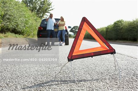 Couple Broken Down On Country Road With Hazard Warning Sign In Foreground