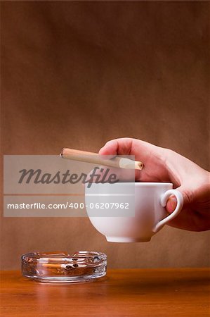 Hand holding a cigarette and a cup ashtray.