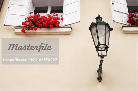 Vintage lantern near open windows with red flowers on the wall of dwelling house