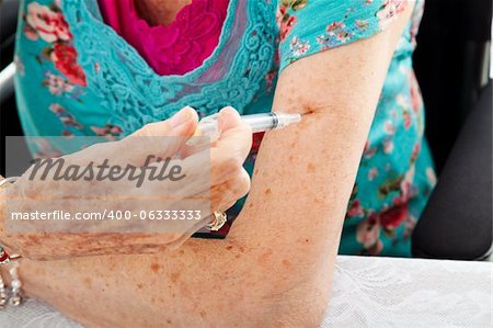 Closeup of a senior woman's hands as she gives herself a shot in the arm.