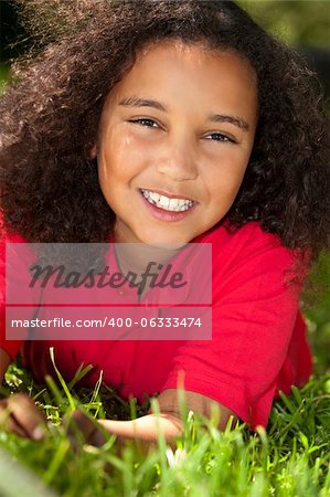 Portrait photograph of a beautiful young smiling happy mixed race interracial African American girl, shot outside in a park on the grass