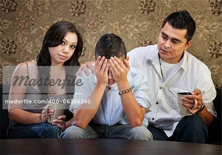 Latino parents comforting sad male teenager with hands in face