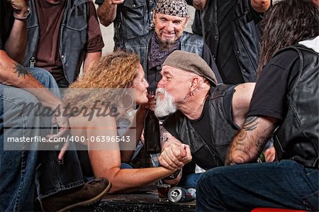 Two biker gang lovers kiss while arm wrestling