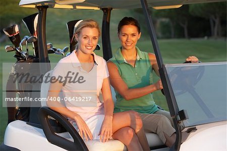 Two Female Golfers Riding In Golf Buggy On Golf Course