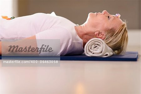 Senior woman relaxing and lying on pad with amethyst, quartz and other crystals on body. Side view, copy space