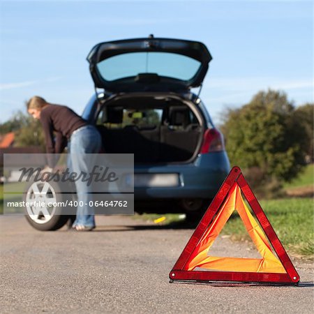 Changing the tire on a broken down car on a road with red warning triangle