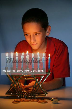 Young boy looking at the Hanukkah menorah, illuminated only by its light.