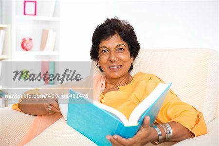 Mature 50s Indian woman reading a book at home