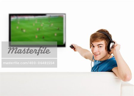Young man sitting on the couch using a remote control and watching a football game on tv