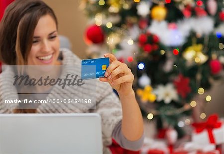 Closeup on credit card in hand of happy woman with laptop near Christmas tree