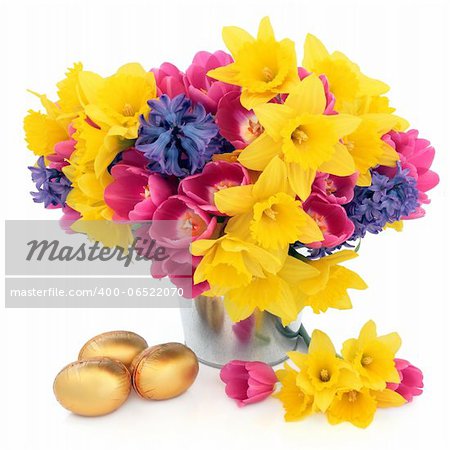 Tulip, daffodil and hyacinth flower arrangement in a metal vase with chocolate golden easter egg group over white background.