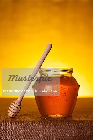Honey jar with dipper on table, canvas background