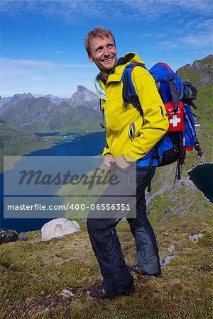 Young smiling active man with backpack hiking on picturesque Lofoten islands in Norway on sunny day