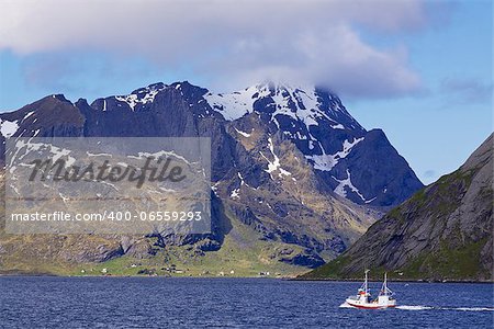 Small fishing boat sailing into scenic fjord on Lofoten islands in Norway