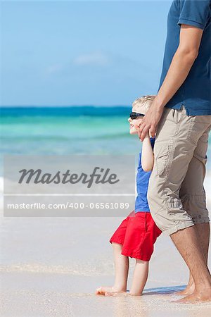 little kid barefoot at the perfect beach together with his father