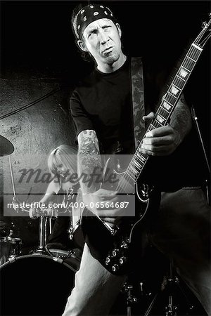 Photo of a female drummer and male guitarist playing on a stage. Slight motion blur on performers.