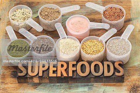 superfoods word in letterpress wood type with plastic scoops of healthy seeds and powders (chia, flax, hemp, pomegranate fruit powder, wheatgrass, maca root)